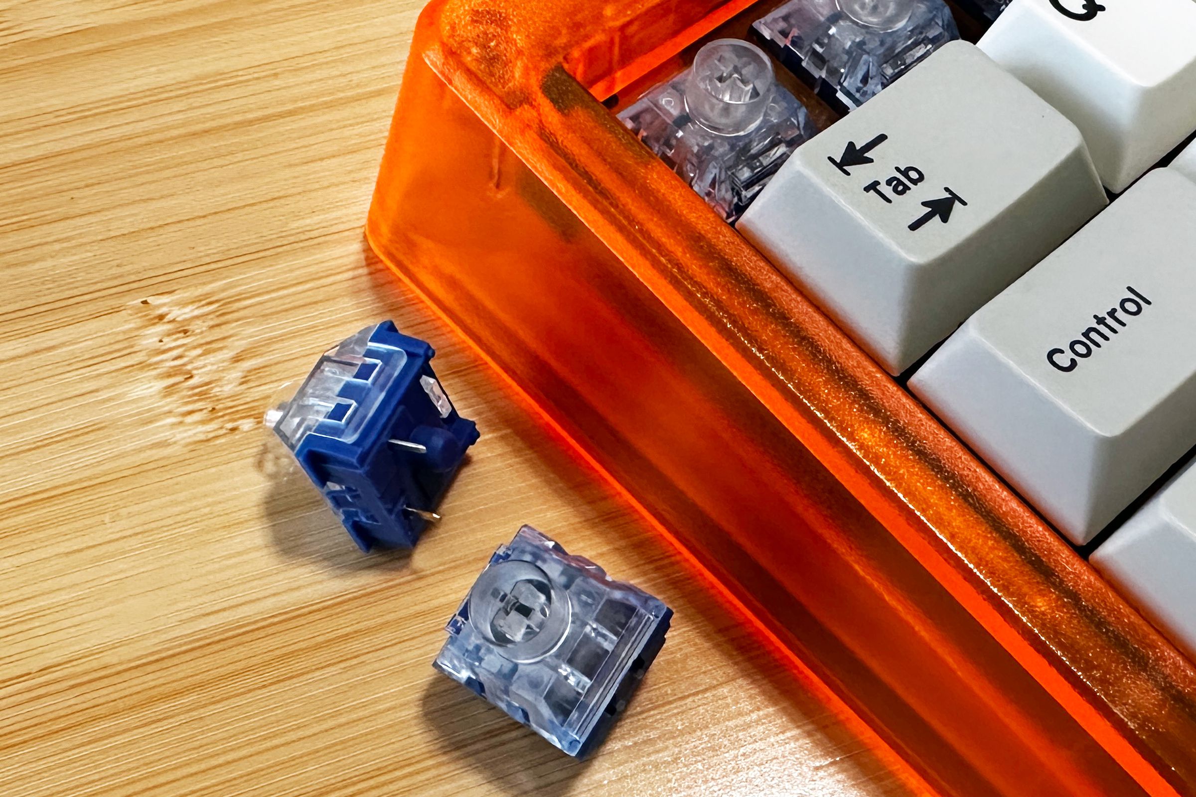 Close up of mechanical keyboard switches with clear tops and blue bases next to a bright orange keyboard. 