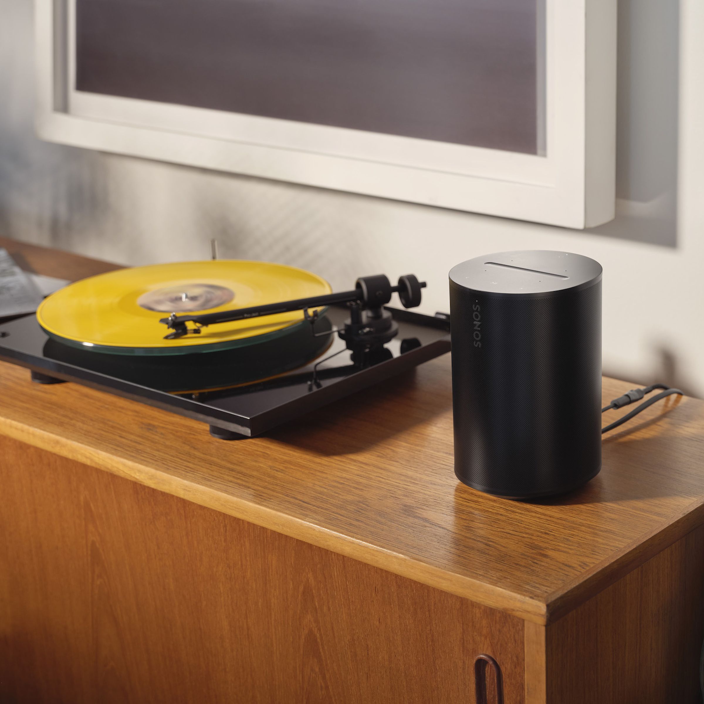 A photo of a Sonos Era 100 beside a turntable.